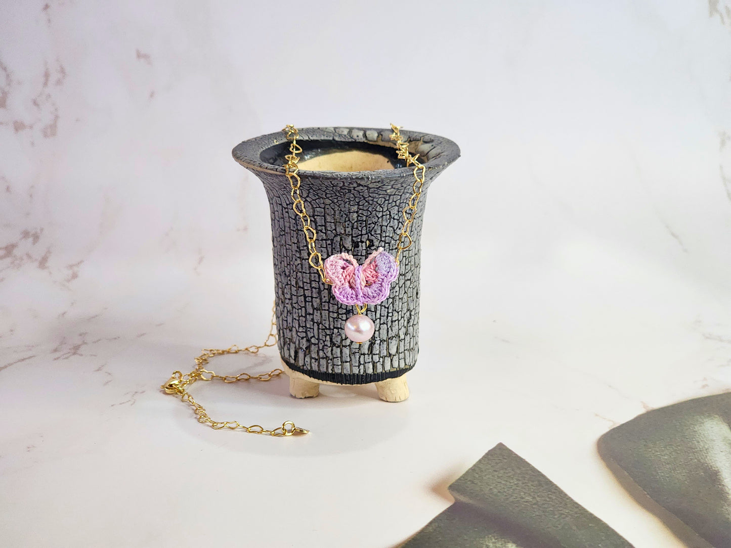 Handcrafted micro-crochet butterfly adorned with an 8mm purple freshwater pearl. Set on 14K gold-filled heart-shaped necklace.