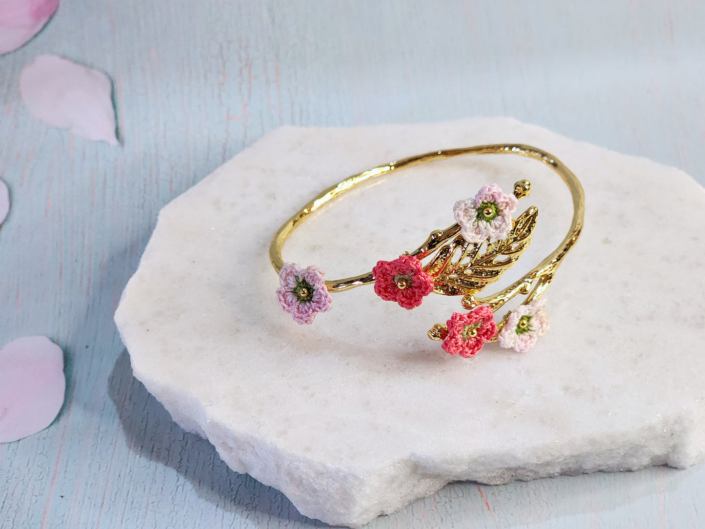 Handcrafted pink and red micro-crochet apple blossoms on an 18K gold-plated leaf bangle.