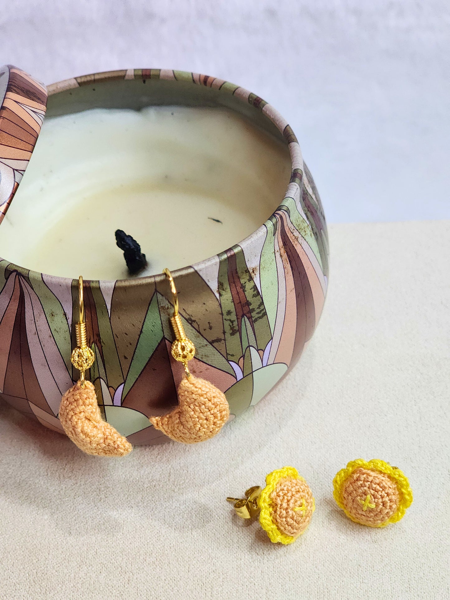 Handcrafted micro-crochet fortune cookie earrings dangling from 18K gold-plated ear hooks