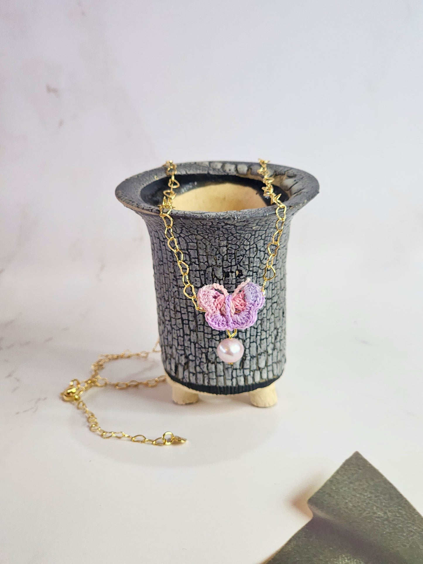 Handcrafted micro-crochet butterfly adorned with an 8mm purple freshwater pearl. Set on 14K gold-filled heart-shaped necklace.