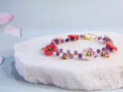 Natural Amethyst crystal bracelet with handcrafted pink and red micro-crochet apple blossoms on an 18K gold-plated chain. With 18K gold-plated enamel hearts.