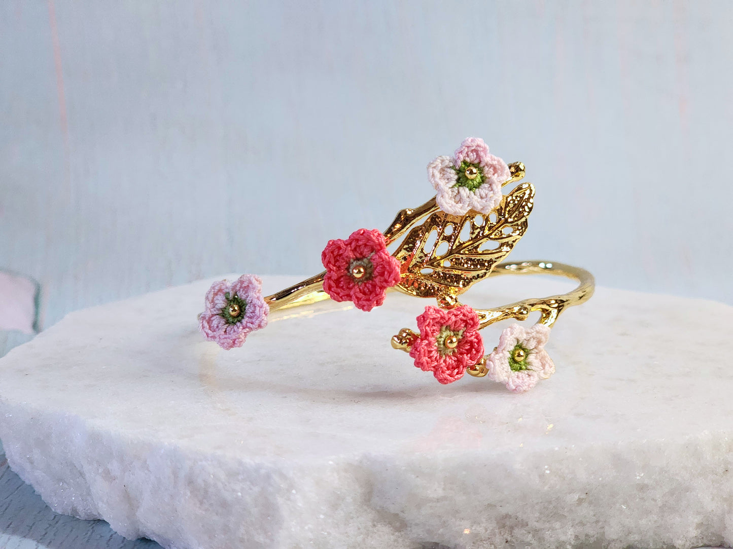 Handcrafted pink and red micro-crochet apple blossoms on an 18K gold-plated leaf bangle. 