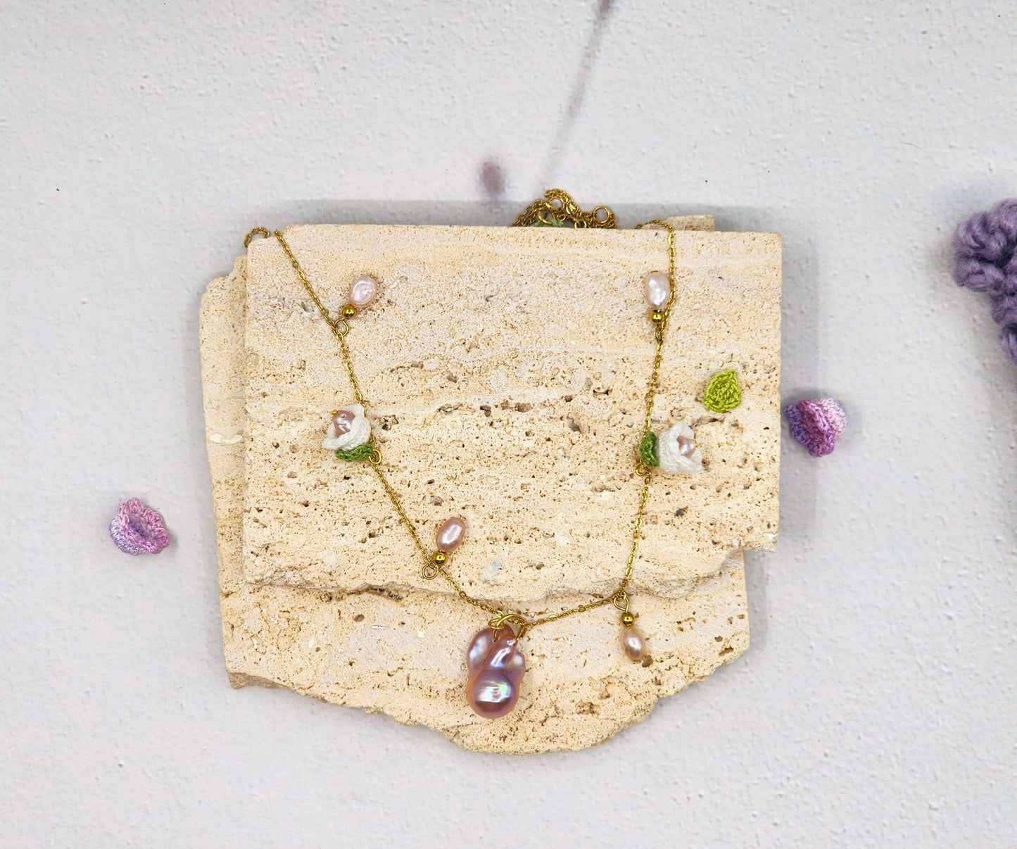 Handcfrafted vintage-style necklace featuring a centrepiece purple-pink metallic Baroque pearl, flanked by pink baroque pearls and micro crochet white lily of the valley blooms. 18K gold-plated titanium stell chain.