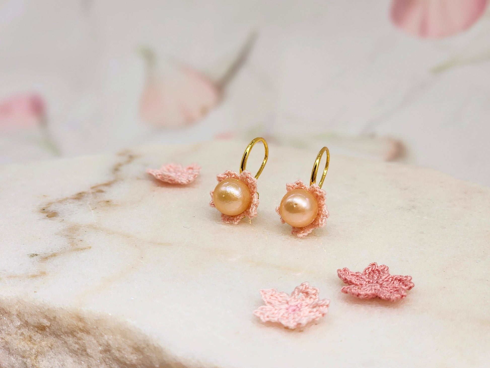 Luminous pink-orange Edison pearls nestled within delicate micro crochet Sakura blossoms. Styled with 18K gold-plated lace motif hooks. 
