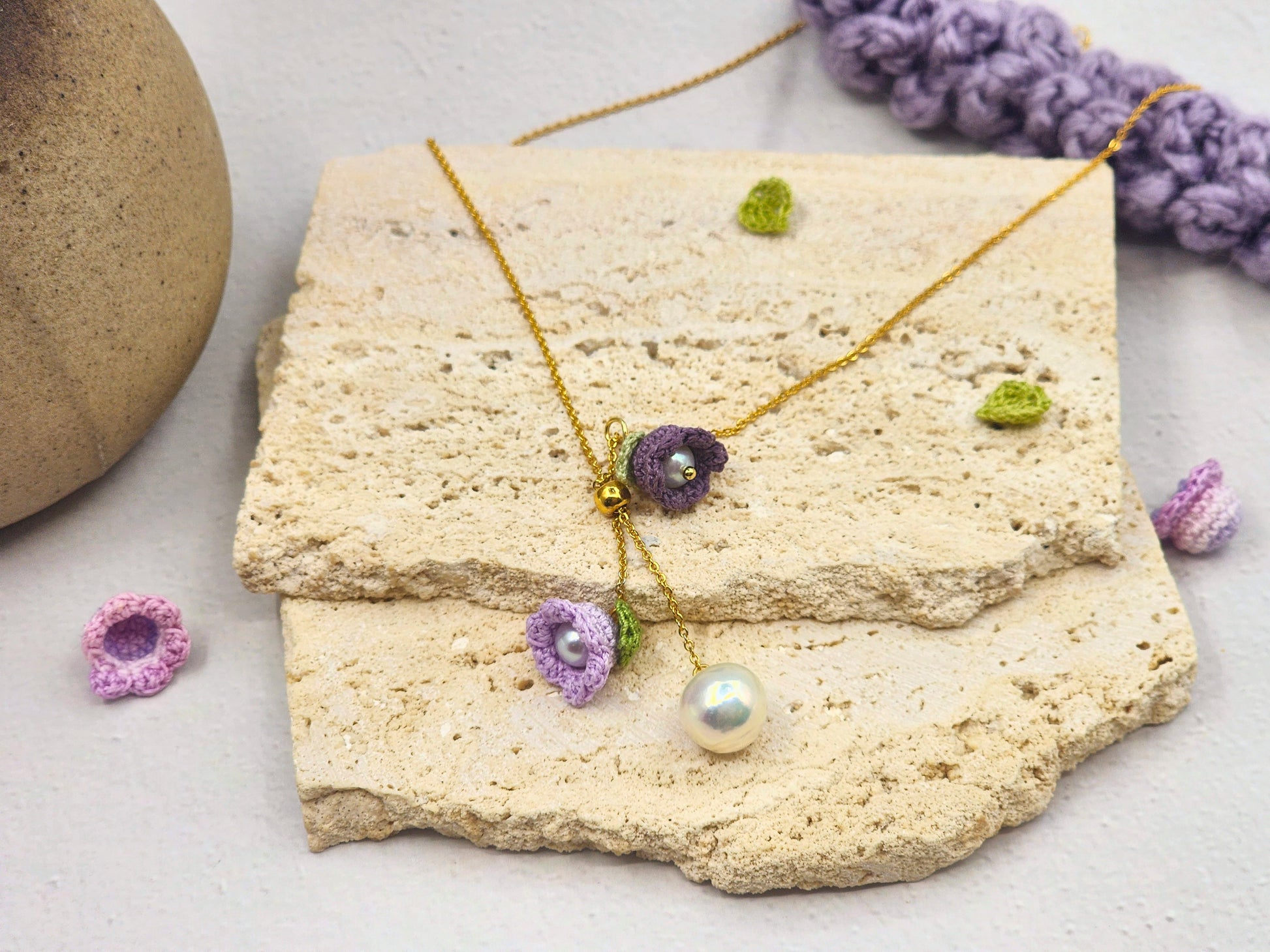 Handcrafted necklace featuring a centre hanging 10mm freshwater Baroque pearl flanked by purple micro crochet Lily of the Valley blooms crowned with 6mm Aurora pearls. 18K gold-plated chain. 
