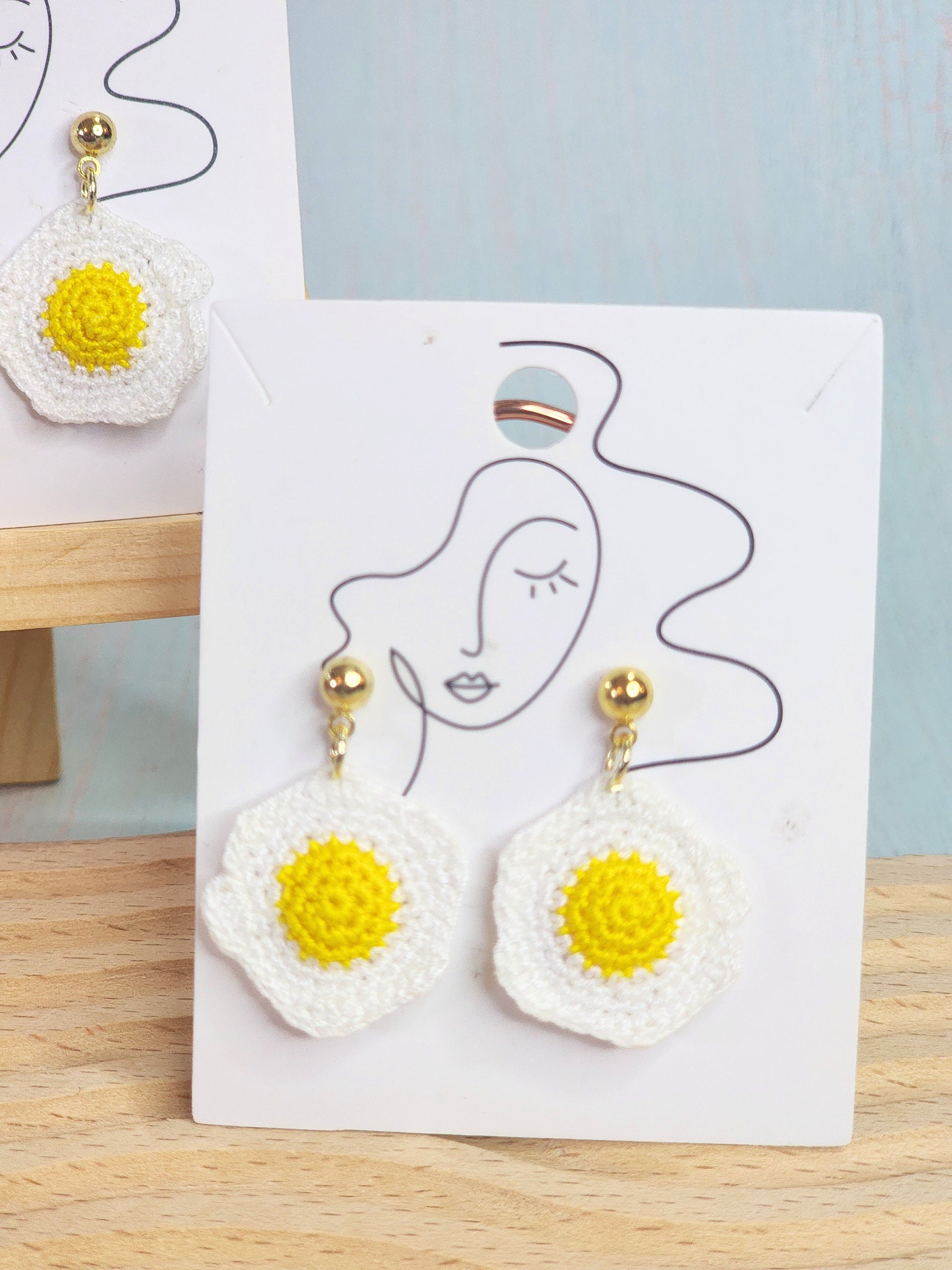 Up close image of a cute & whimiscal fried egg micro-crochet earrings. Handcrafted with ultra-fine lace yarn and paired with sterling silver hooks