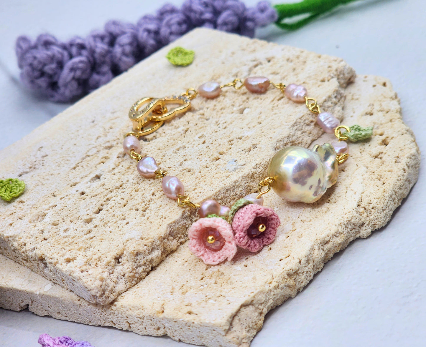 Handcrafted micro crochet Lily of the Valley blooms bracelet. Delicate 4-5mm pink-purple freshwater Baroque pearls decorate an 18K gold-plated chain. At its heart sits an exceptional > 10mm Baroque pearl. 