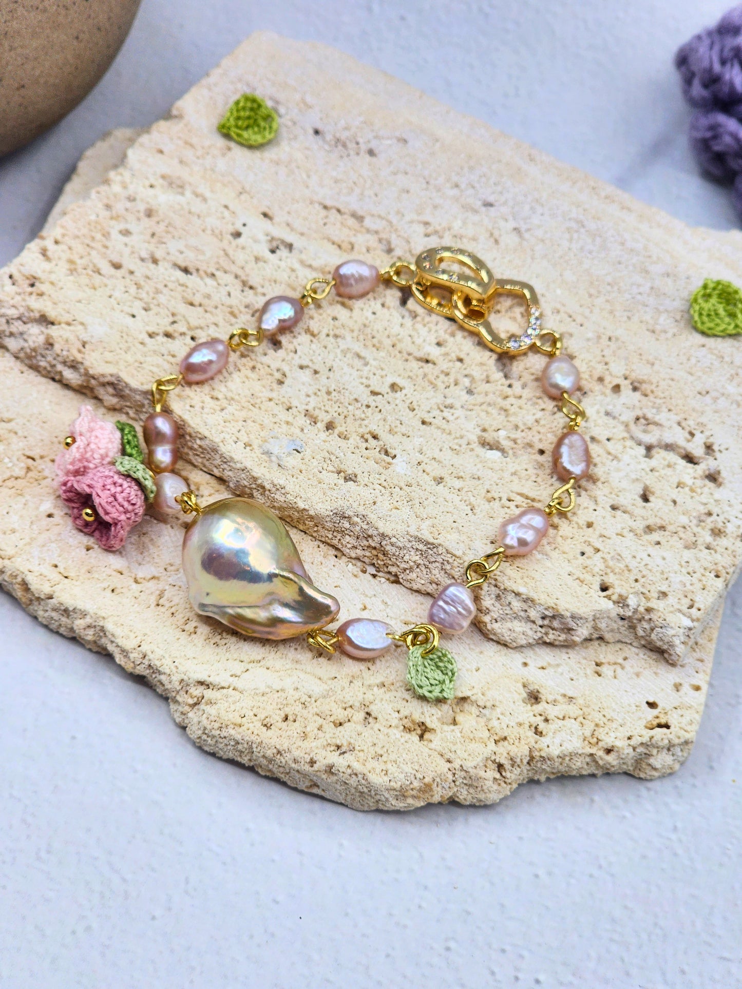 Handcrafted micro crochet Lily of the Valley blooms bracelet. Delicate 4-5mm pink-purple freshwater Baroque pearls decorate an 18K gold-plated chain. At its heart sits an exceptional > 10mm Baroque pearl. 