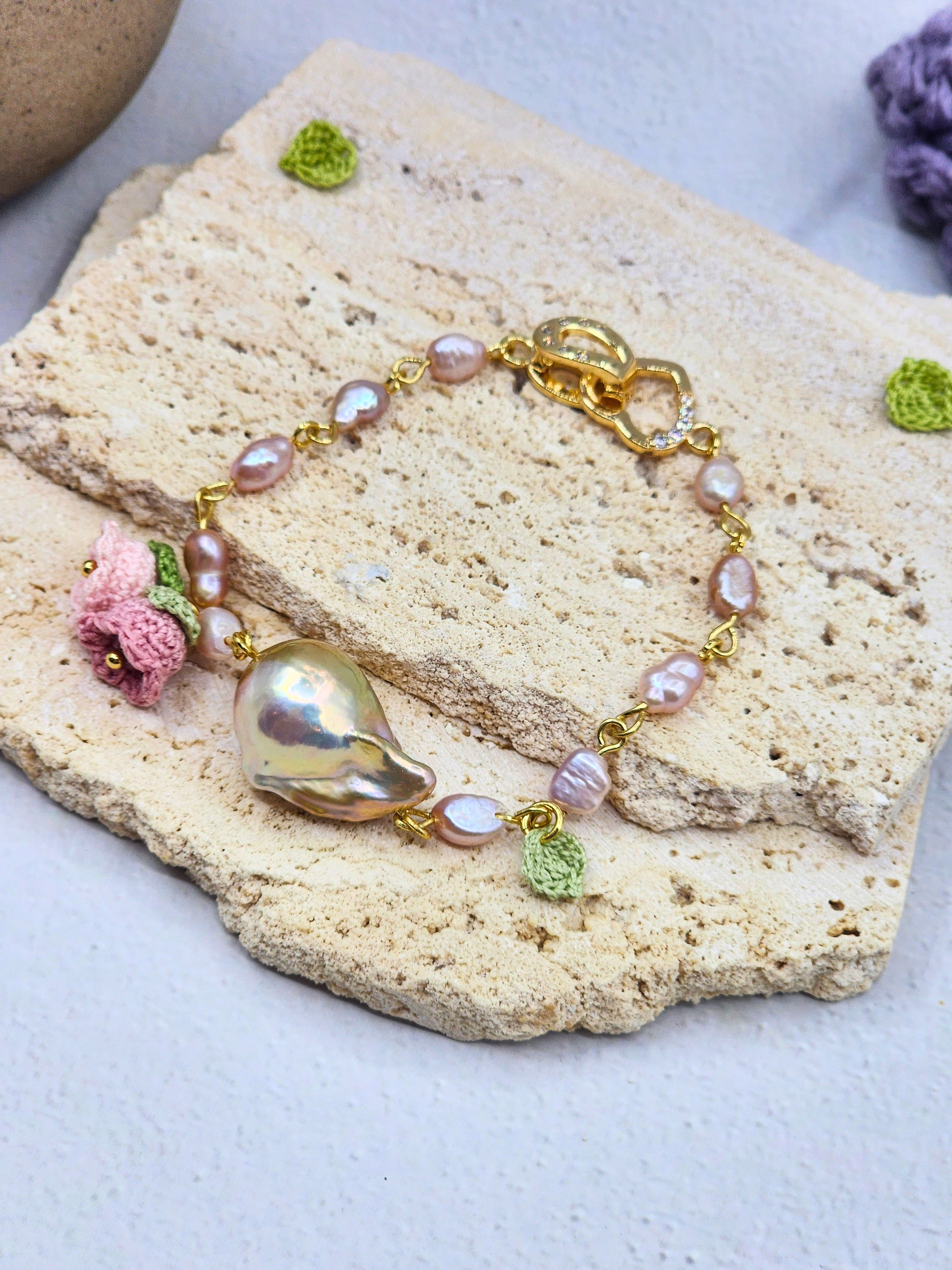 Handcrafted micro crochet Lily of the Valley blooms bracelet. Delicate 4-5mm pink-purple freshwater Baroque pearls decorate an 18K gold-plated chain. At its heart sits an exceptional > 10mm Baroque pearl. 