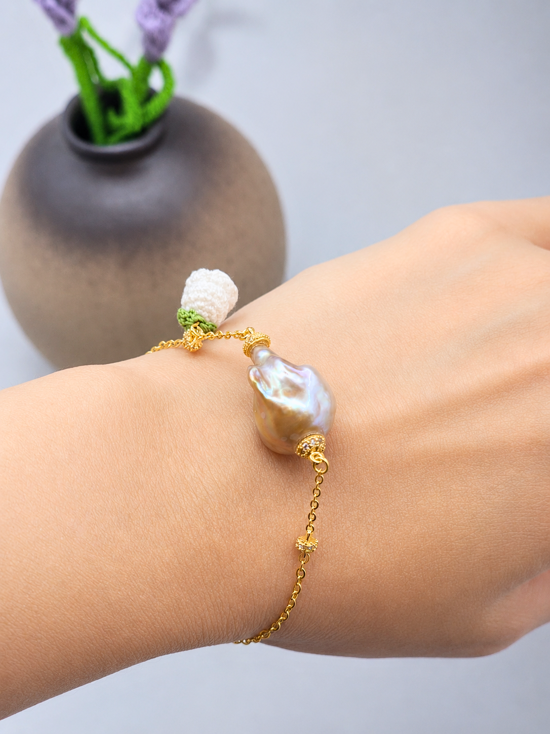Exceptional metallic baroque pearl bracelet with handcrafted white micro crochet Lily of the Valley bloom. Sparkling cubic zirconia accents on an 18K gold-plated chain. 