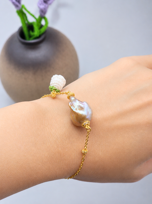 Exceptional metallic baroque pearl bracelet with handcrafted white micro crochet Lily of the Valley bloom. Sparkling cubic zirconia accents on an 18K gold-plated chain. 